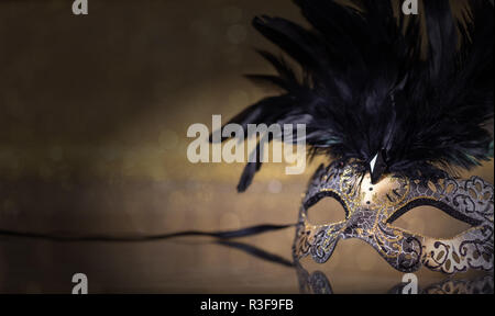 Karneval. Venezianische Maske mit Federn auf dunklen goldenen Hintergrund, Reflexionen, Kopie Raum Stockfoto