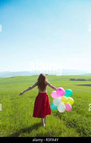 Happy girl In den Wiesen der Toskana mit bunten Luftballons, gegen den blauen Himmel und grüne Wiese. Toskana, Italien Stockfoto