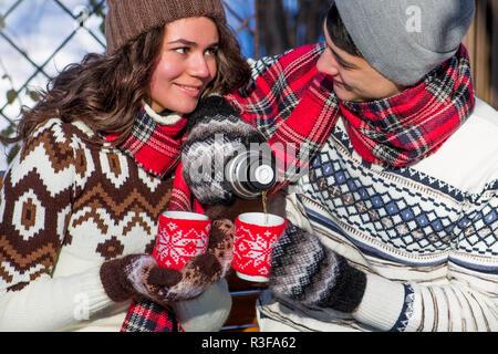 Junges Paar gießt heißen Tee aus der Thermoskanne im Winter Wald Stockfoto