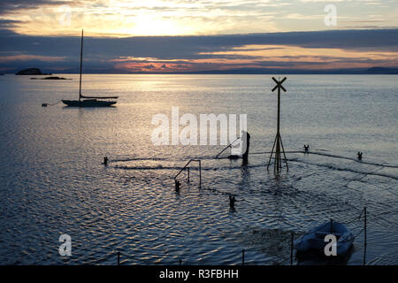 Sonnenuntergang über erhabene North Berwick. Alte Pier nur sichtbar als Flut deckt Oberfläche. Fischer steht auf alte Pier. Stockfoto