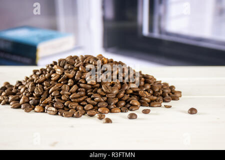 Menge ganze dunkle braune Bohnen süß Arabica mit Büchern in der Nähe der Fenster im Hintergrund Stockfoto