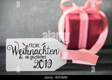 Etikett mit Deutschen Kalligraphie Frohe Weihnachten und ein Glueckliches 2019 bedeutet, frohe Weihnachten und einen guten Rutsch ins Jahr 2019. Ein rosa Geschenk mit Ribbn. Zement Bac Stockfoto