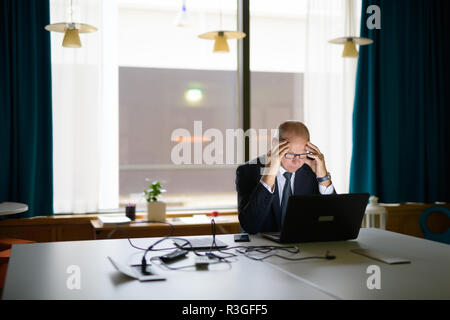 Betonte älterer Geschäftsmann Arbeiten mit Laptop beim Sitzen im Büro Stockfoto