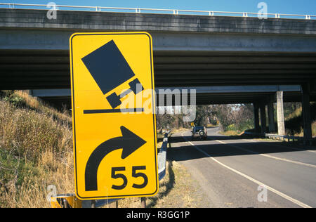 Ein Schild warnt FAHRER DIE GESCHWINDIGKEIT VERRINGERN, WIE EINE KURVE IN DER STRASSE ANSÄTZE (Ill. von BEIM KIPPEN), New South Wales, Australien Stockfoto