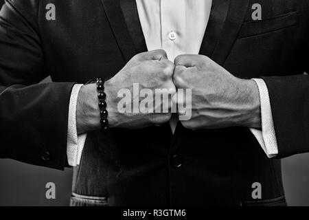 Geschäftsmann ballte die Fäuste, versteckte Aggression Konzept. Mann in smart Anzug und weißes Hemd. Bürokauffrau auf dunklem Hintergrund. Guy tragen Perlen bracele Stockfoto