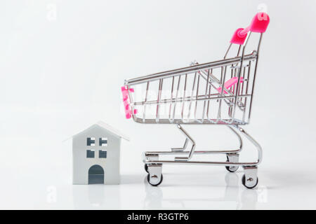 Entwerfen Sie einfach mit Miniatur white toy House, Supermarkt Lebensmittelgeschäft Schubkarre für den Einkauf auf weißem Hintergrund. Hypothek Sachversicherung dre Stockfoto