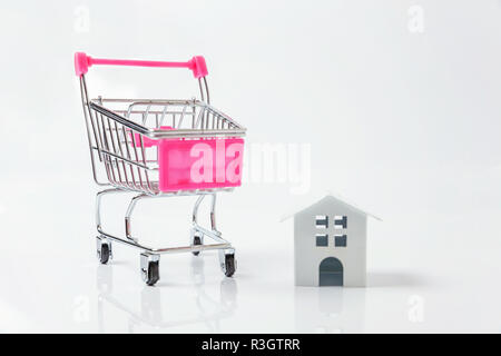 Entwerfen Sie einfach mit Miniatur white toy House, Supermarkt Lebensmittelgeschäft Schubkarre für den Einkauf auf weißem Hintergrund. Hypothek Sachversicherung dre Stockfoto