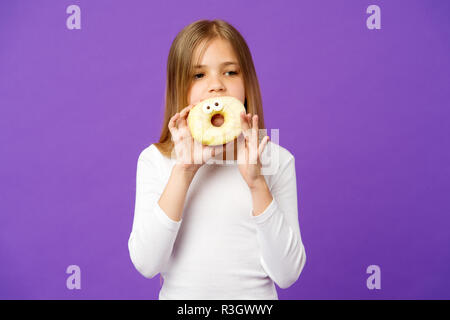 Mädchen, dass große Krapfen mit Puderzucker. Süßes, verglaste Bagel mit Augen. Kind essen lustig Dessert, süße Kindheit. Kind mit langem Haar zu tragen whi Stockfoto