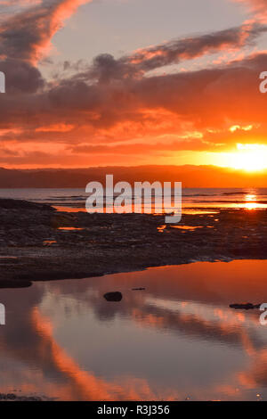 Eine brennende orange Sonnenuntergang im Rock Pools entlang der Strand von Gisborne, Neuseeland wider. Stockfoto