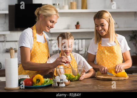 Glückliches Kind mit Mutter und Großmutter Kochen Gemüse Salat zusammen in der Küche Stockfoto