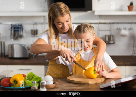 Lächelnden jungen Frau helfen kleine Tochter schneiden Pfeffer in der Küche Stockfoto