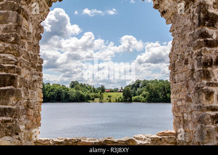Blick auf das Landhaus am Ufer des Flusses durch die Ruinen von Koknese Schloss - eine der größten und bedeutendsten mittelalterlichen Burgen auf Lettisch territor Stockfoto