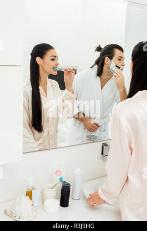 Schöne Frau Zähneputzen und gutaussehenden Mann rasieren vor dem Spiegel im Bad Stockfoto