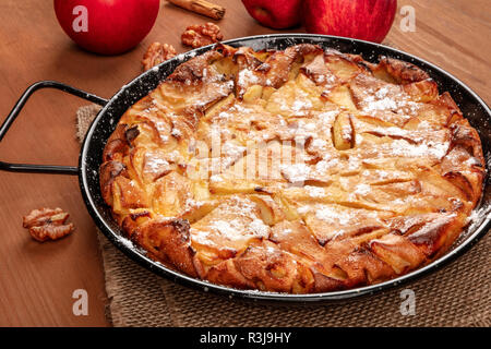 Ein Foto eines Apfelkuchen in der Pfanne, auf einem dunklen Holzmöbeln im Landhausstil Hintergrund mit Äpfeln und Walnüssen Stockfoto