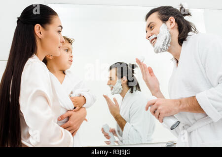 Lächelnder Mann mit Schaum im Gesicht mit Frau und Sohn in Bad Stockfoto