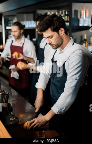 Stattliche Barkeeper Schürze slicing Grapefruit mit Messer am Zähler Stockfoto