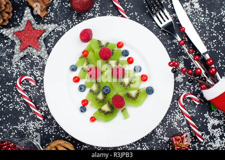 Genießbare Weihnachtsbaum von Kiwi Slices auf einer schwarzen Platte über Dunkle Schiefer, Stein oder Beton Hintergrund Stockfoto