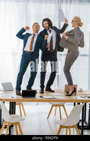 Freudige Versicherung der Arbeitnehmer tanzen auf dem Tisch in der Sitzung im Amt Stockfoto