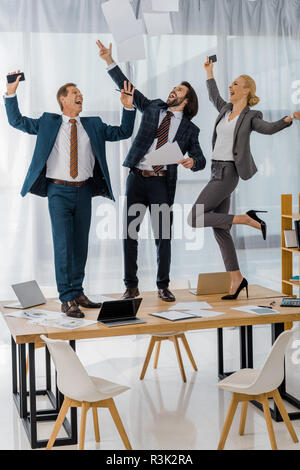 Freudige Versicherung der Arbeitnehmer Tanz auf den Tisch und werfen Papiere bei den Treffen im Büro Stockfoto