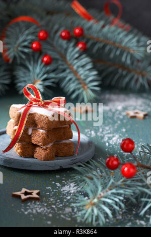 Stapel von Christmas Star cookies gebunden Markröhre red ribbon auf Grün und Rot festliche Hintergrund mit grünen Zweigen Tanne mit roten Beeren dekoriert Stockfoto