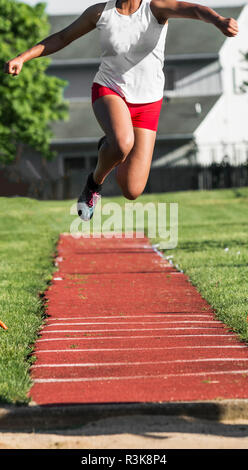 Ein High School weiblichen lange Brücke wird hoch in die Luft in Richtung der Sand während einer Leichtathletik Wettbewerb im Freien. Stockfoto