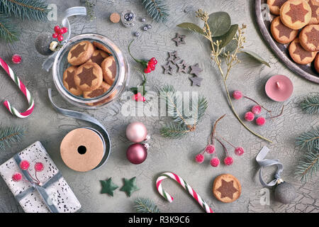 Weihnachten Kekse mit Schokolade star Pattern mit verschiedenen Weihnachten Dekorationen und Zuckerstangen. Flach in Grün und Rosa auf dunklen Holzmöbeln im Landhausstil backgrou Stockfoto