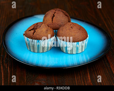 Home gebackene Kakao Muffins auf einem hellen blauen Platte, auf einem dunkelbraunen Holz Brett angeordnet Stockfoto
