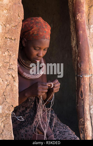 Junge Mutter webt Seil in der Eingang ihrer Hütte, innen ein Himba Dorf in der Nähe von Opuwo, Namibia. Stockfoto