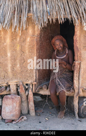 Junge Mutter webt Seil in der Eingang ihrer Hütte, innen ein Himba Dorf in der Nähe von Opuwo, Namibia. Stockfoto