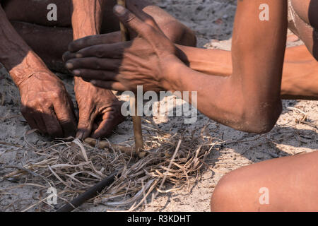 Zwei San Buschmänner arbeiten zusammen, um ein Feuer im Busch den manuellen Weg zu beginnen, im östlichen Namibia, Afrika. (Redaktionelle nur verwenden) Stockfoto