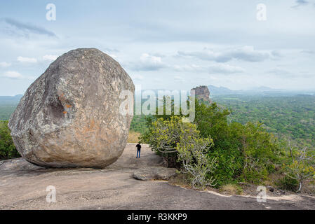 Eine Person, die die Ansichten der Lion Rock in Sigiriya hinter einem Felsen von Pidurangala, Sri Lanka Stockfoto