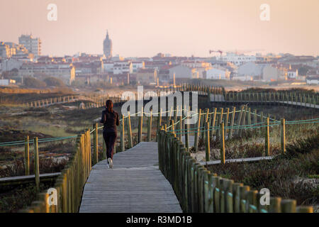 Junges Mädchen läuft auf der Promenade inmitten der Vegetation auf dem Weg zu weit entfernten Stadt. Kaukasische, dunkle Haare, schwarze Trainingsanzug. Ansicht von hinten. Kopieren Sie Platz. Klaren Tag. Warme li Stockfoto