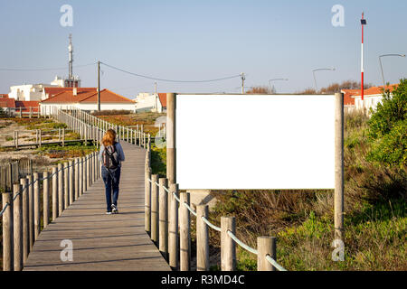 Junge rothaarige Frau geht durch eine Werbung mit Reklametafeln mockup auf einer Promenade inmitten der Vegetation. Rucksack. Ansicht von hinten. Kopieren Sie Platz. Stockfoto