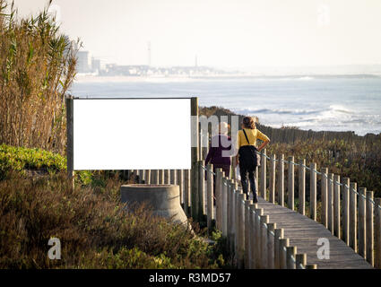 Zwei ältere Frauen gehen durch eine Werbung mit Reklametafeln mockup auf einer Promenade in der Nähe des Meeres. Ansicht von hinten. Kopieren Sie Platz. Stockfoto
