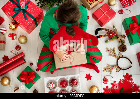 Neugierige Junge tragen xmas Schlafanzug sitzen auf dem Boden und öffnete seine Weihnachtsgeschenk, Ansicht von oben. Stockfoto