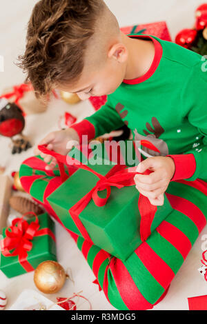 Neugierige Junge tragen xmas Schlafanzug sitzen auf dem Boden und öffnete seine Weihnachtsgeschenk, Ansicht von oben. Stockfoto