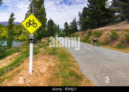 Schild und Radfahrer auf der Alpen zu Ocean Cycle Trail am Lake Aviemore, Canterbury, Südinsel, Neuseeland Stockfoto