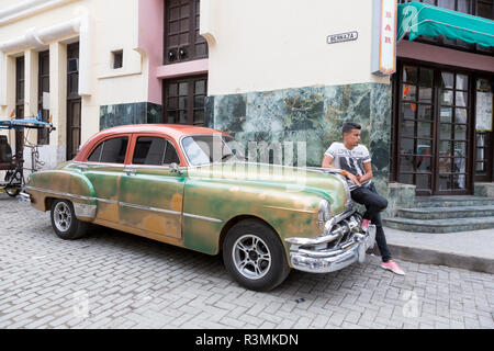 Kuba, Havanna, Havanna. Junger Mann lehnte sich auf seinen Oldtimer. Kredit als: Wendy Kaveney/Jaynes Galerie/DanitaDelimont.com Stockfoto