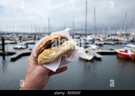 Mann hält Burger weiter in Großbritannien während Stumpf bewölkten Tag marina Stockfoto