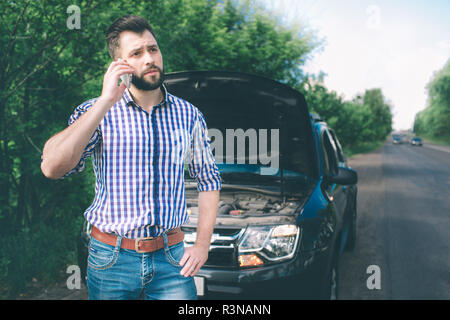 Ein junger Mann mit einem schwarzen Auto, die unten auf der Straße brach. Er fordert der Techniker zu gelangen. Stockfoto