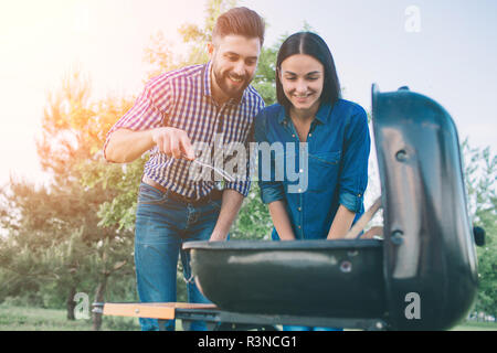 Freunde Grill und dem Mittagessen in der Natur. Paar Spaß beim Essen und Trinken zu einem Pic-nic - glückliche Leute an der Grillparty Stockfoto