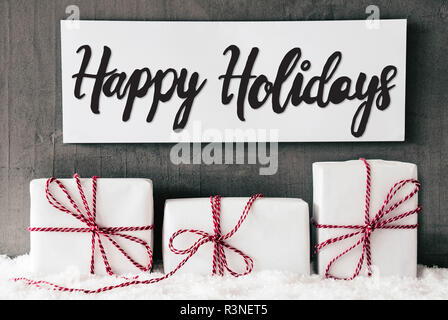 Mit englischen Kalligraphie Happy Holidays unterzeichnen. Drei weiße Geschenke mit roten Ribbn. Grau Grungy Zement Hintergrund mit Schnee Stockfoto