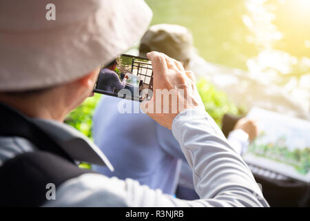 Alter Mann reisen mit Rucksack in Park und ein Foto von Zeichnung Künstler, der die Aussicht auf Park, smart phone in Park Stockfoto