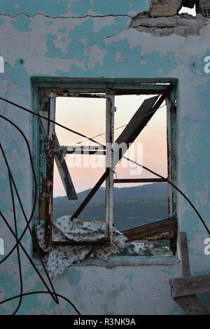 Gebrochene Fenster in verlassenen Haus mit Verfilztem verrostete Drähte und fernen Bergblick während der blauen Stunde. Stockfoto