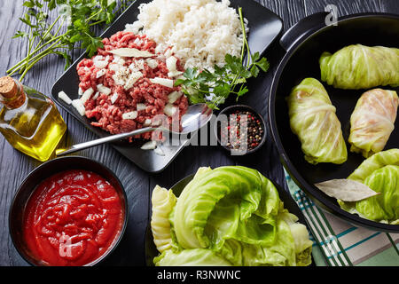 Ungekocht gefüllte Kohlblätter mit Zutaten - Hackfleisch, gekochtem Reis, Petersilie und Tomatensauce auf einem schwarzen Tabelle, Ansicht von oben, flatlay, Clos Stockfoto