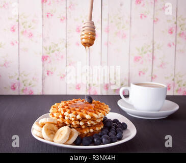 Tasse Kaffee und Waffeln mit Bananen, Blaubeeren und Honig. Frühstück am Morgen. Stockfoto