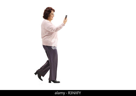 Volle Länge Profil geschossen von einer älteren Dame zu Fuß mit einem Mobiltelefon auf weißem Hintergrund Stockfoto