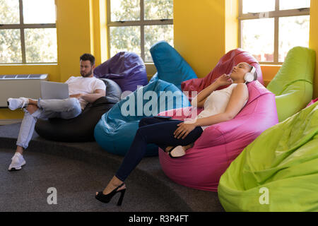 Führungskräfte entspannend und mit Laptop sitzend auf Bean Bag Stockfoto