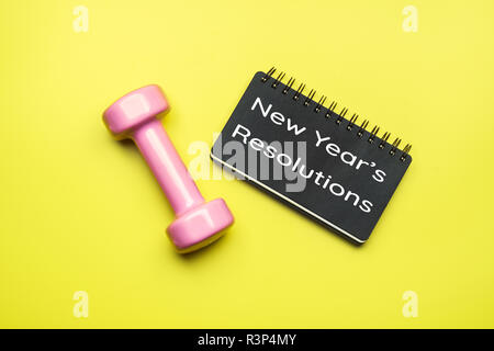 Neue Jahr gesund Ziele und Beschlüsse Konzept. Das neue Jahr Entschließungen auf Schwarz Notebook Papier geschrieben und Hanteln auf gelbem Hintergrund, Fitness, S Stockfoto