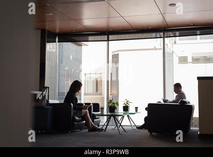 Kaufmann und Kauffrau mit Handy und digitale Tablet-PC in der Lobby Stockfoto